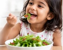 A young girl happily eating a bowl of salad with microgreens